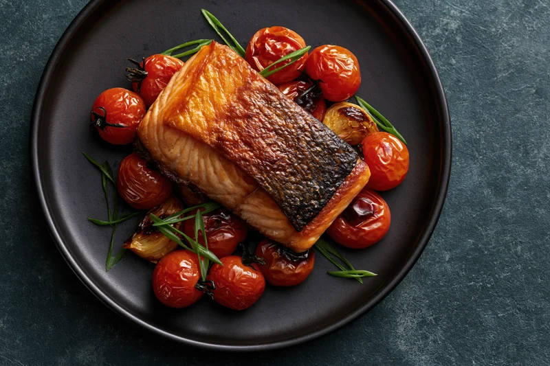 Pan-seared salmon fillet with roasted tomatoes and herbs on a dark matte ceramic plate