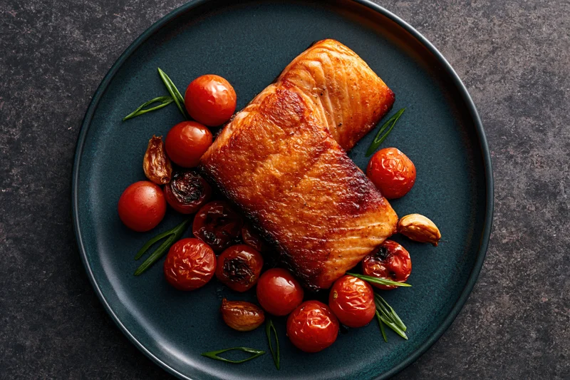 Pan-seared salmon fillet with roasted tomatoes and rosemary on a dark matte ceramic plate