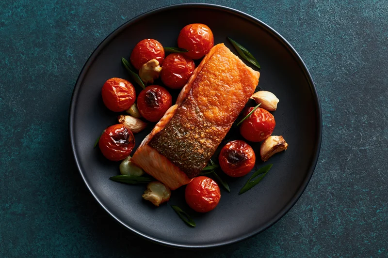 Pan-seared salmon fillet with roasted tomatoes and garlic on a dark matte ceramic plate