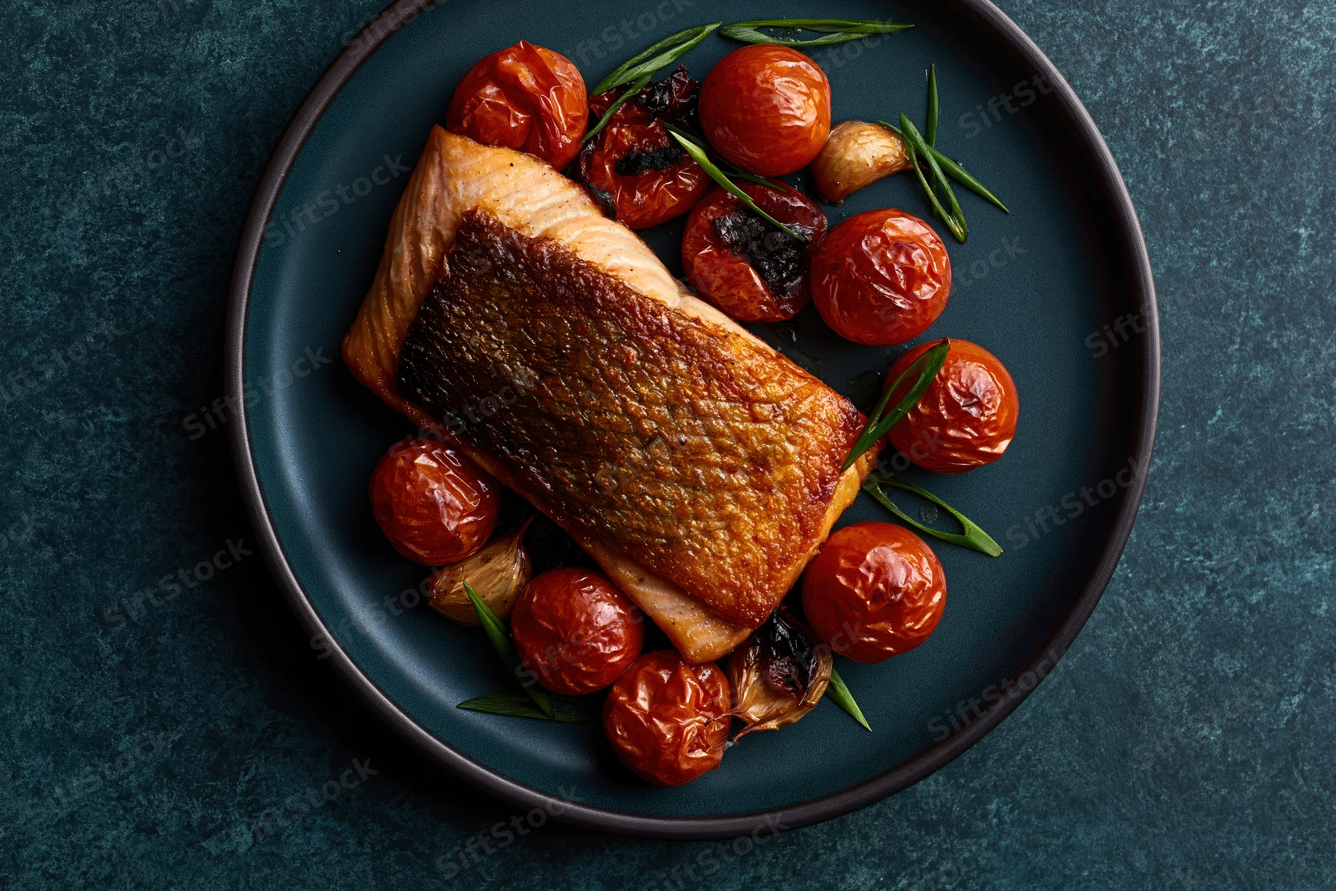 Pan-seared salmon fillet with roasted tomatoes and garlic on a dark matte ceramic plate