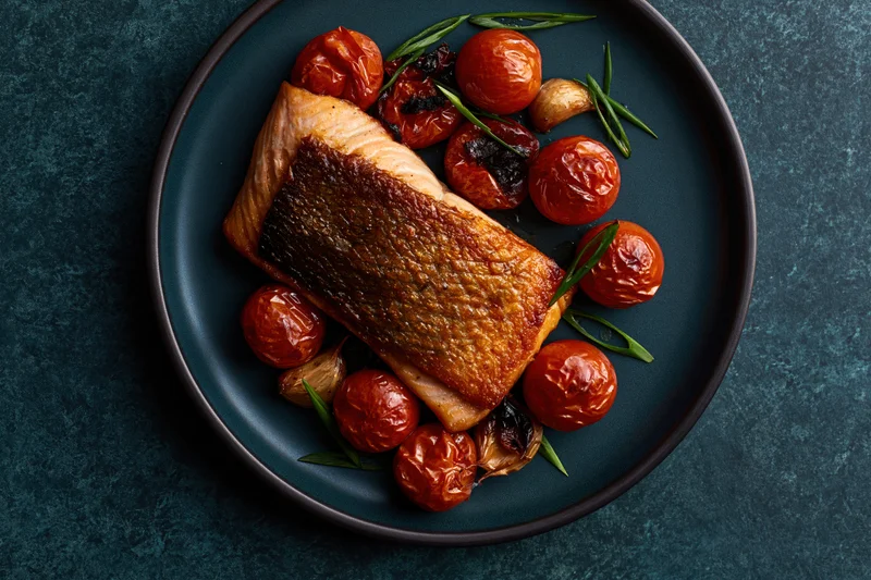 Pan-seared salmon fillet with roasted tomatoes and garlic on a dark matte ceramic plate