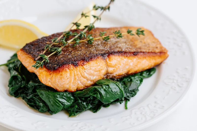 Pan-seared salmon fillet with crispy skin on sautéed spinach on a white plate