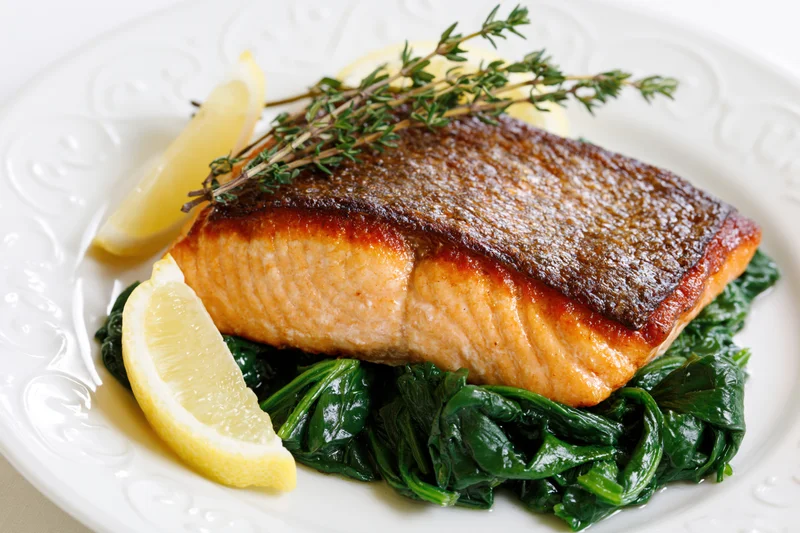 Pan-seared salmon fillet with crispy skin served on spinach with lemon and thyme on a white plate