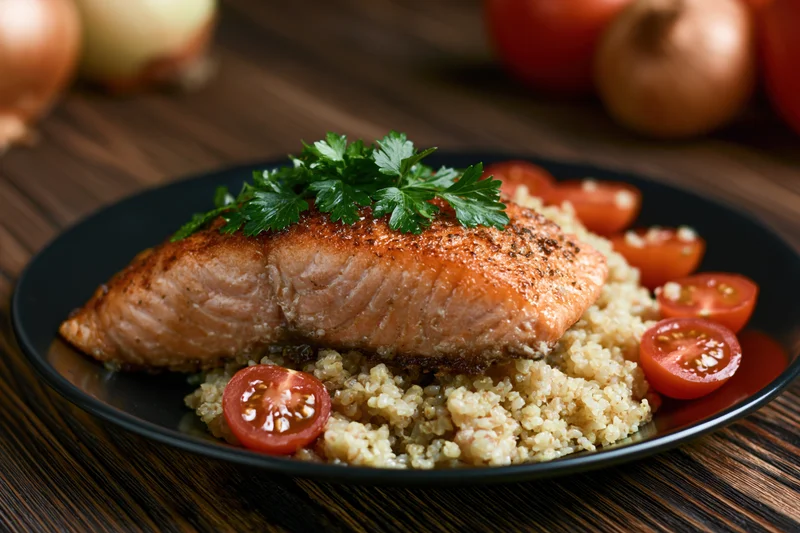 Pan-seared salmon fillet on a bed of quinoa with cherry tomatoes and parsley garnish on a wooden table