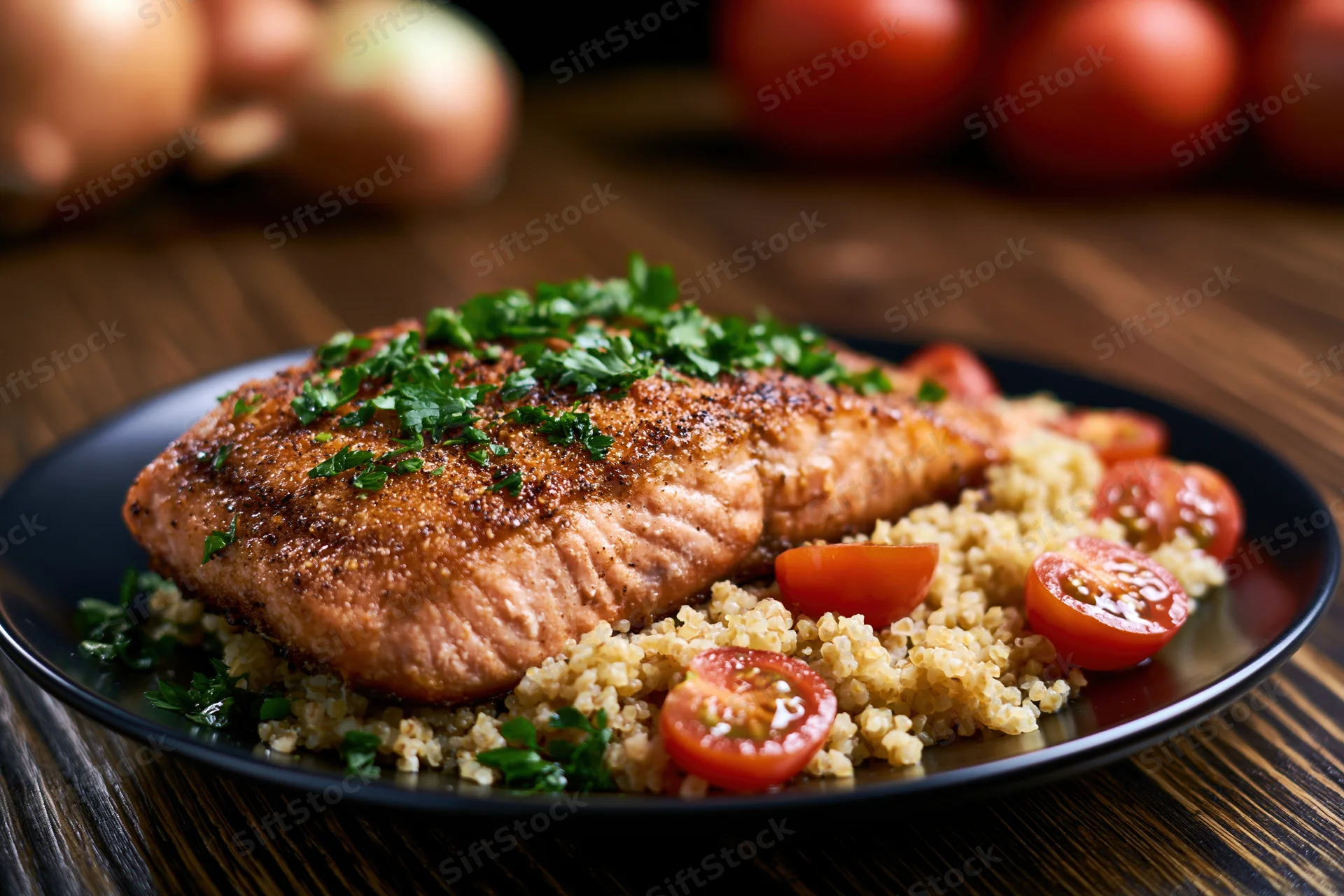 Pan-seared salmon fillet with golden-brown crust served on quinoa with cherry tomatoes and parsley on a black plate on wooden table