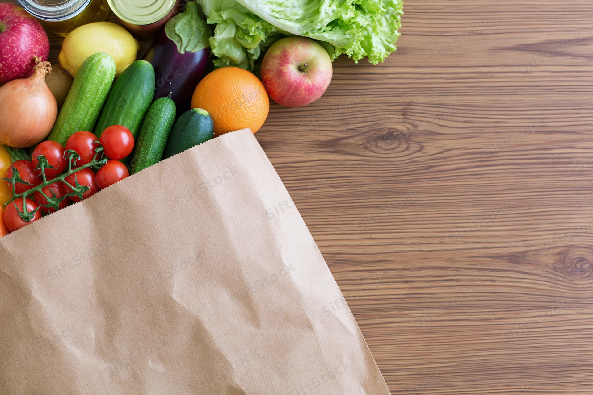 Paper grocery bag tipped on side spilling fresh vegetables and fruits onto wooden table