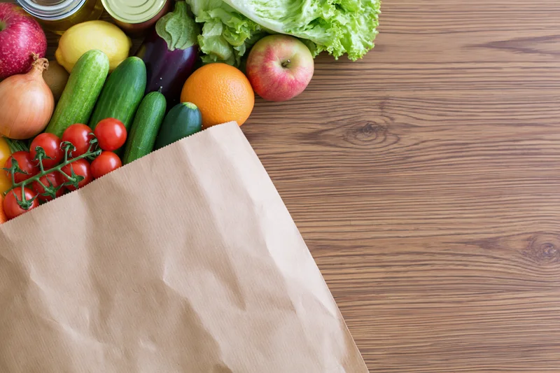 Paper grocery bag tipped on side spilling fresh vegetables and fruits onto wooden table