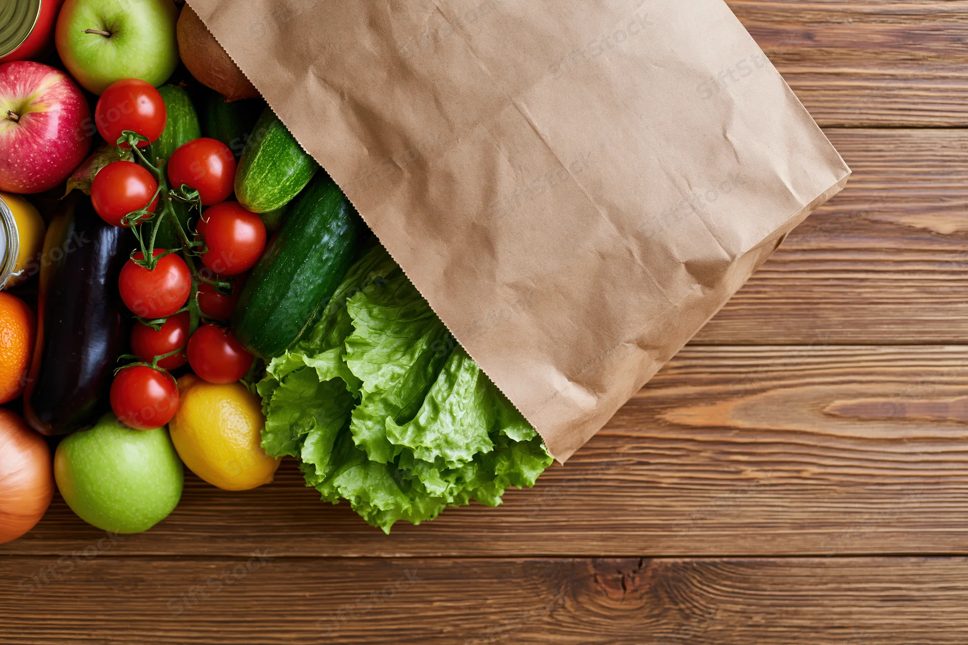 Paper grocery bag tipped on wooden table spilling fresh vegetables and fruits