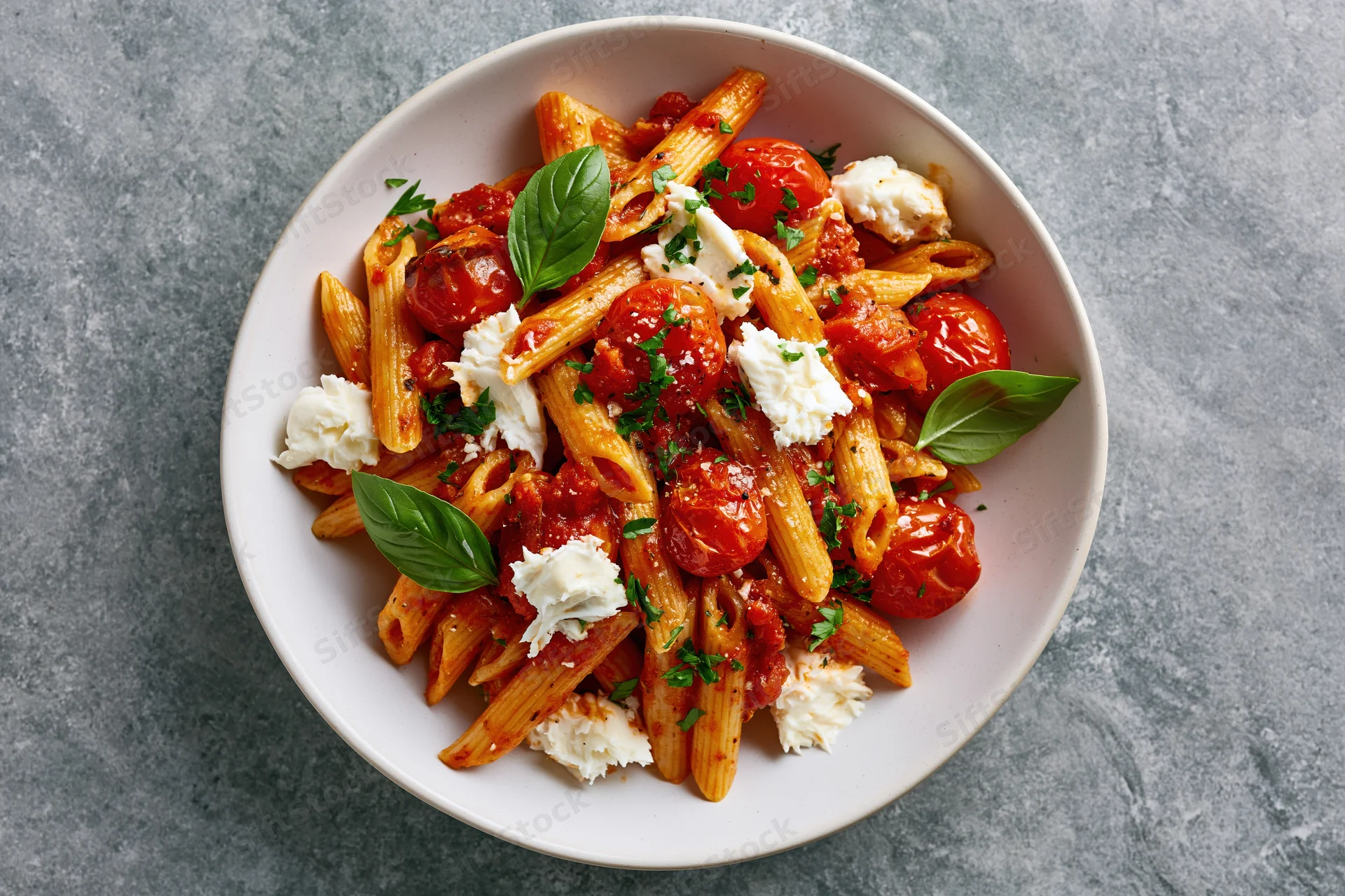 Penne pasta with roasted cherry tomatoes and torn mozzarella in a white bowl on a gray surface