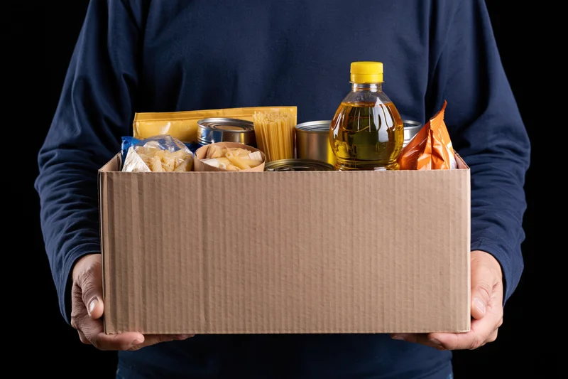 Person holding a cardboard box filled with food pantry donations