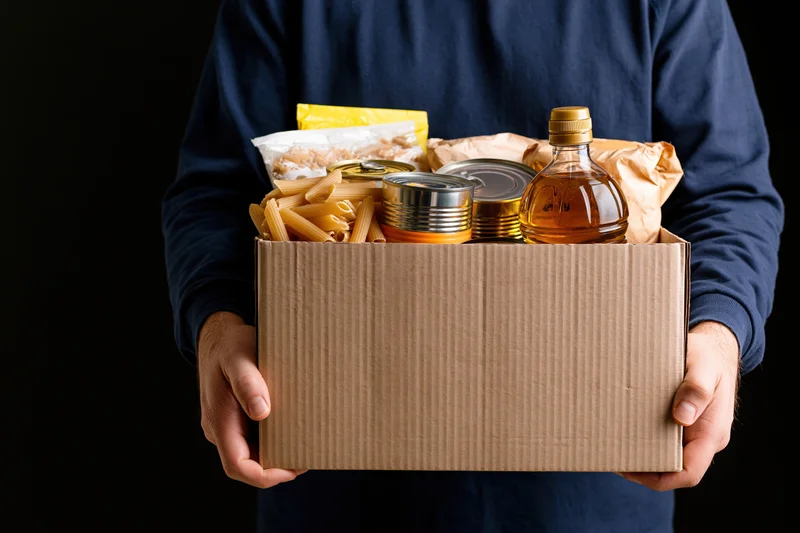Man holding a cardboard box filled with food pantry donations