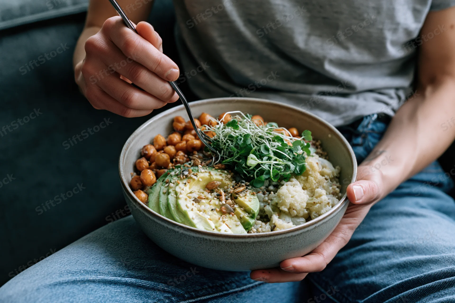 Woman holding a ceramic bowl of vegan grain bowl with avocado and chickpeas on her lap