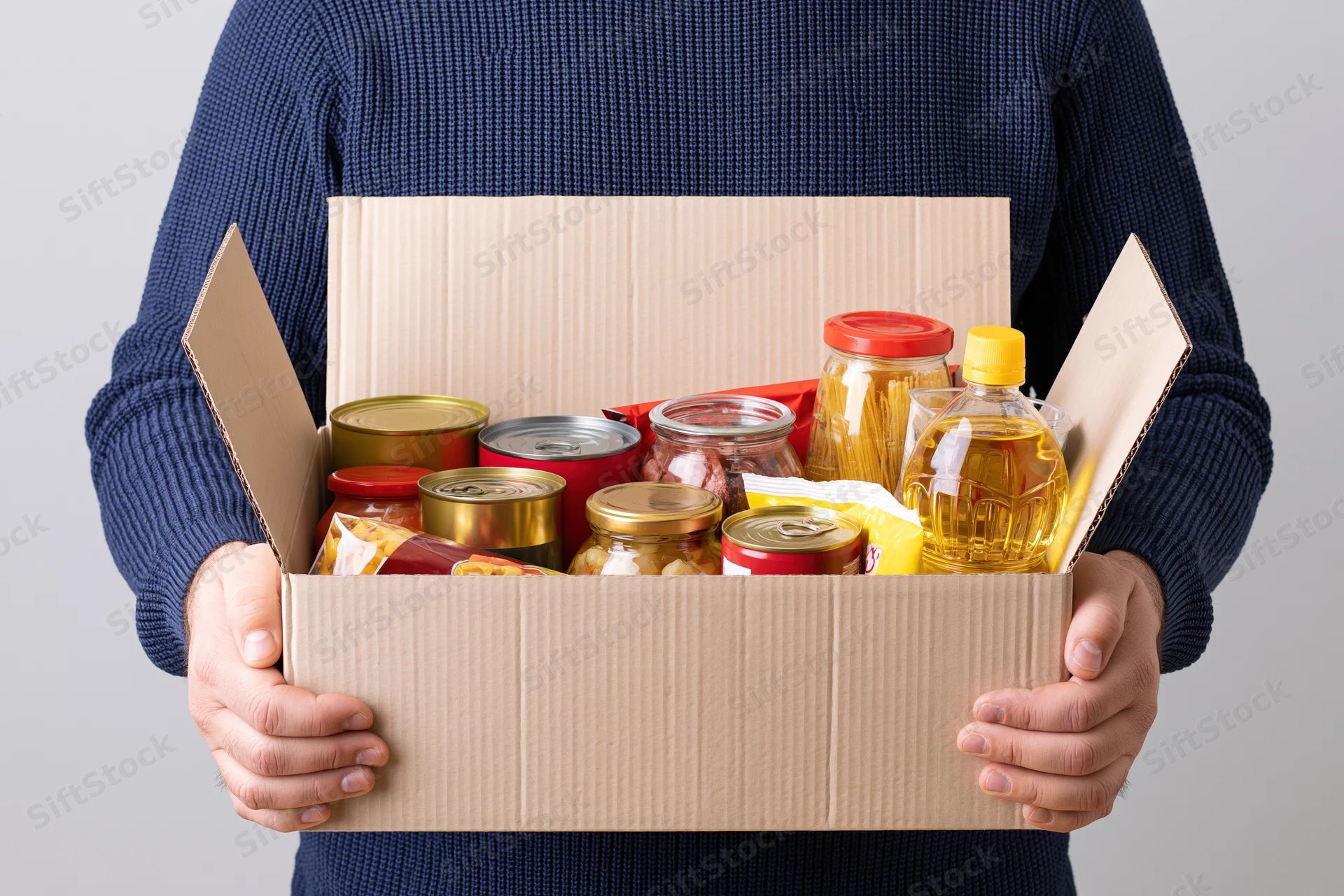 Person holding open cardboard box filled with assorted non-perishable food items
