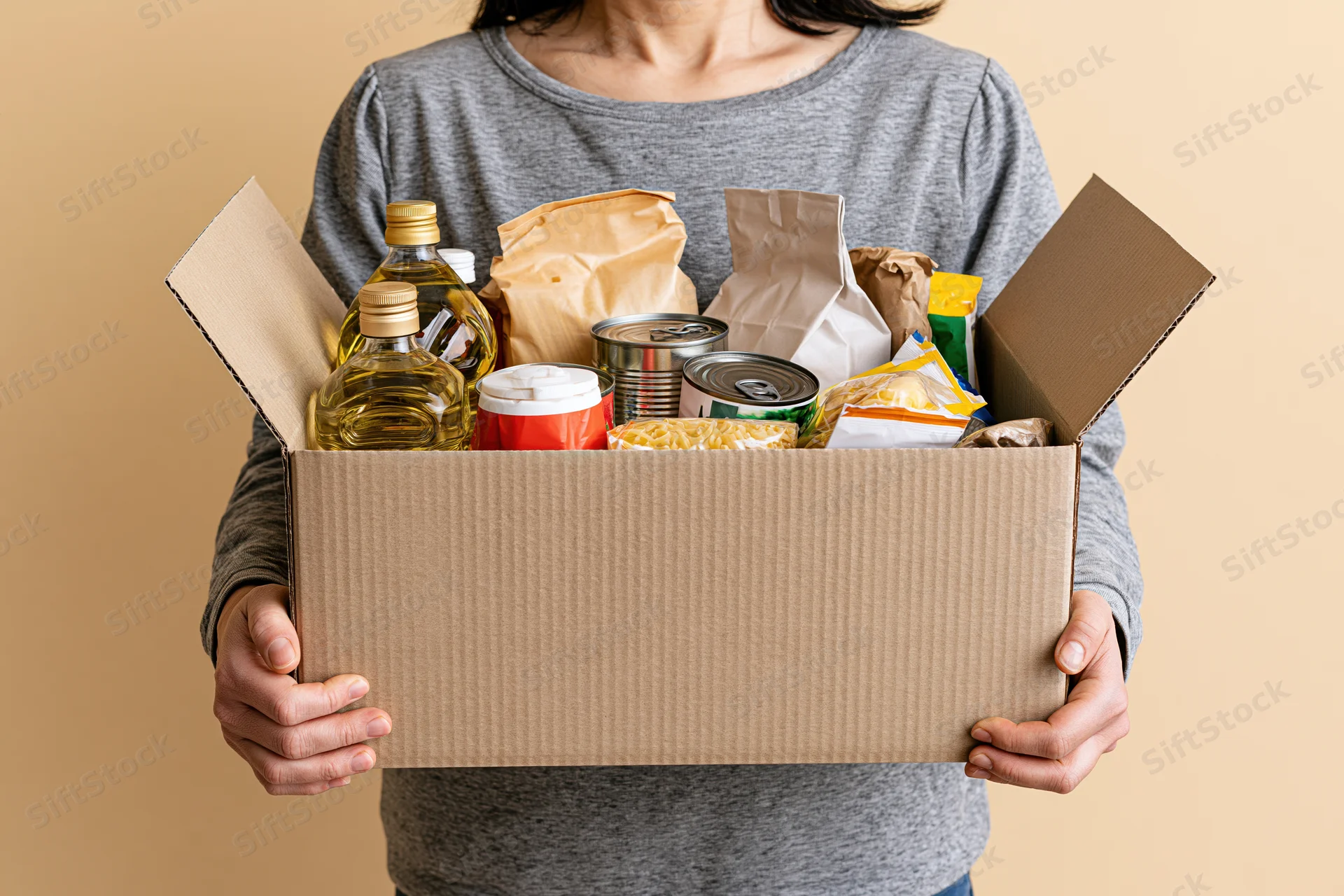 Woman holding open cardboard box filled with pantry staples