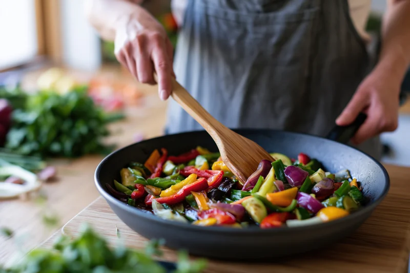 Woman stirring colorful vegetables in a pan on a kitchen counter