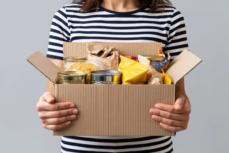 Woman holding open cardboard box filled with canned food and dry goods