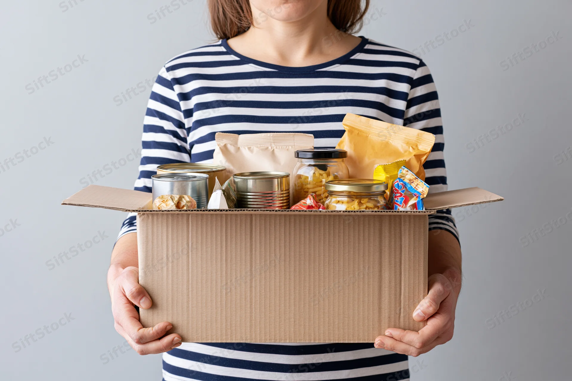 Woman holding open cardboard box filled with canned food and snacks