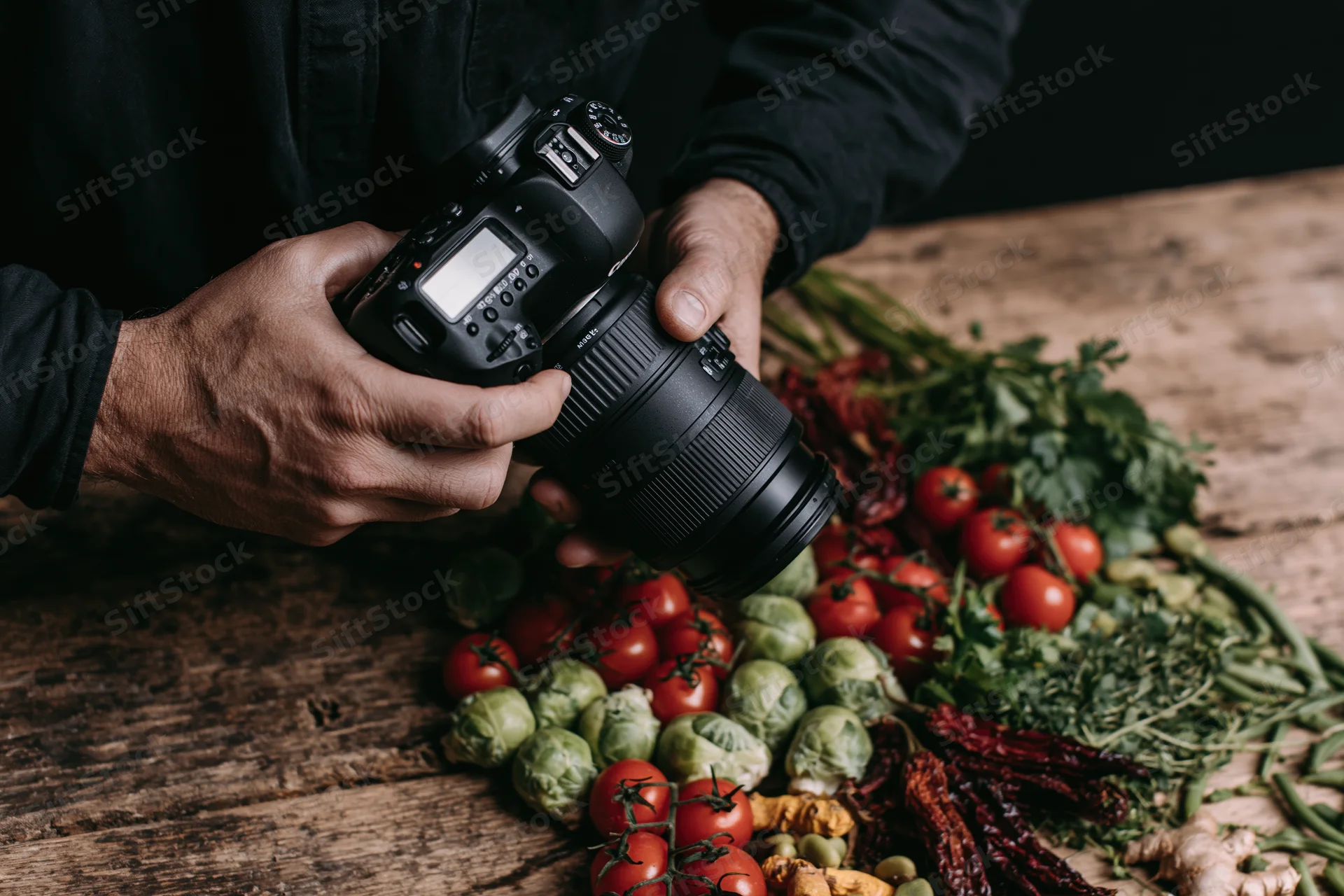 Photographer holding dslr camera over arrangement of fresh vegetables on wooden table