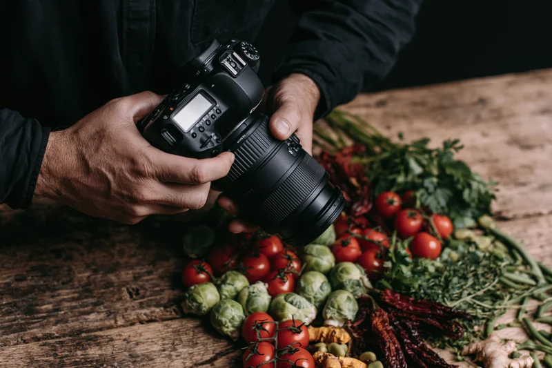 Photographer holding dslr camera over arrangement of fresh vegetables on wooden table