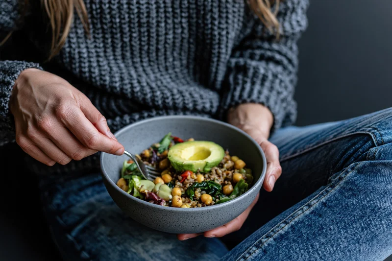Woman eating a bowl of grain salad with avocado and chickpeas while sitting