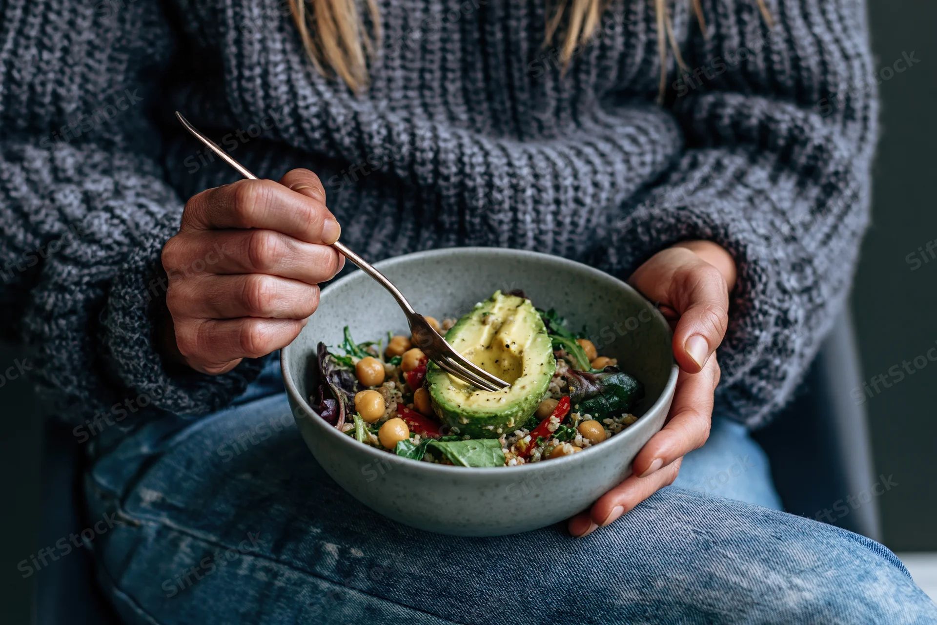 Woman eating a salad with avocado and chickpeas from a ceramic bowl while seated