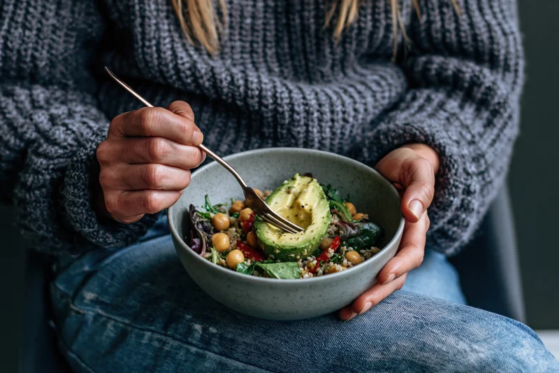 Woman eating a salad with avocado and chickpeas from a ceramic bowl while seated