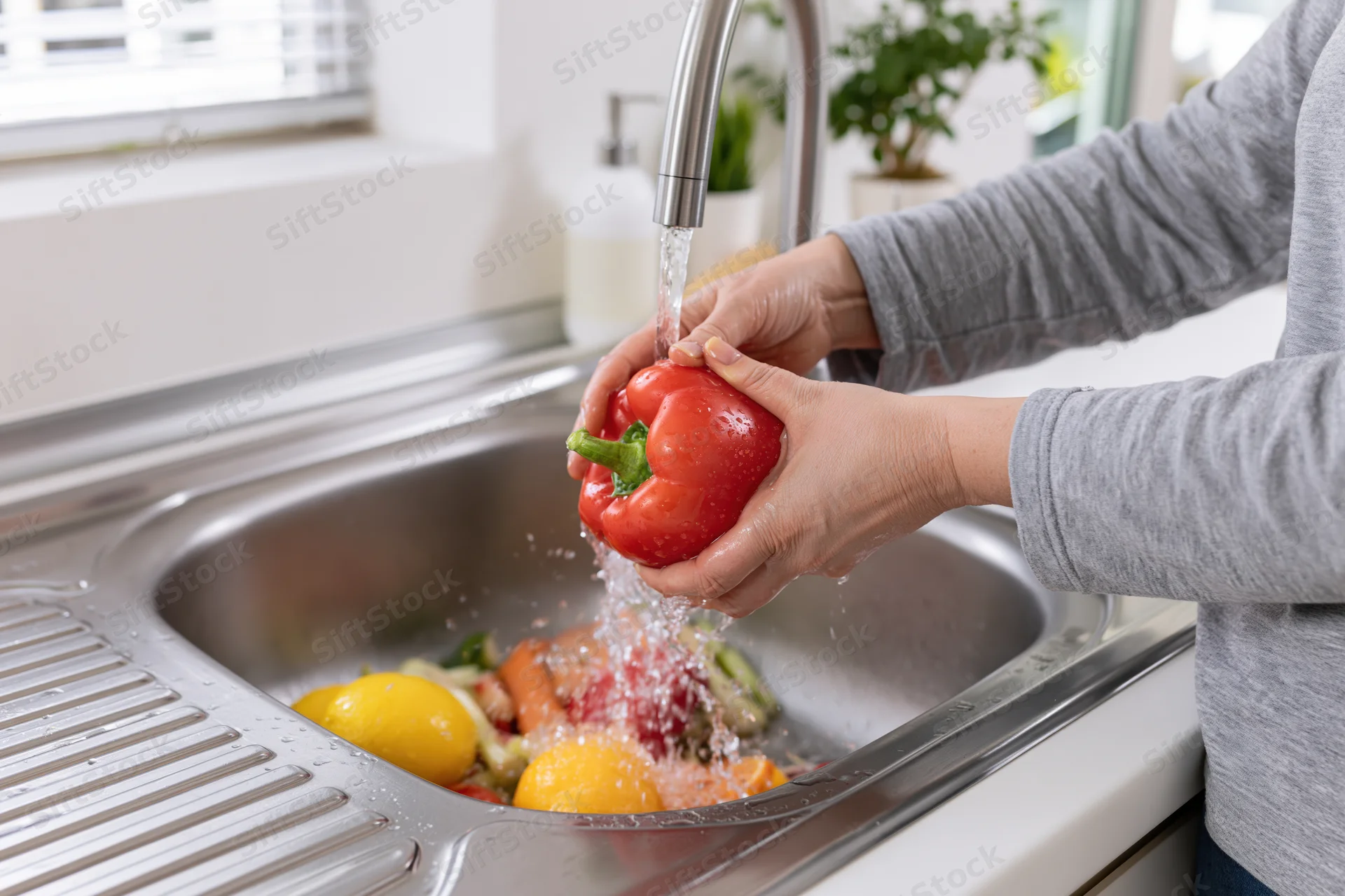 Woman washing a red bell pepper under running tap water in a kitchen sink