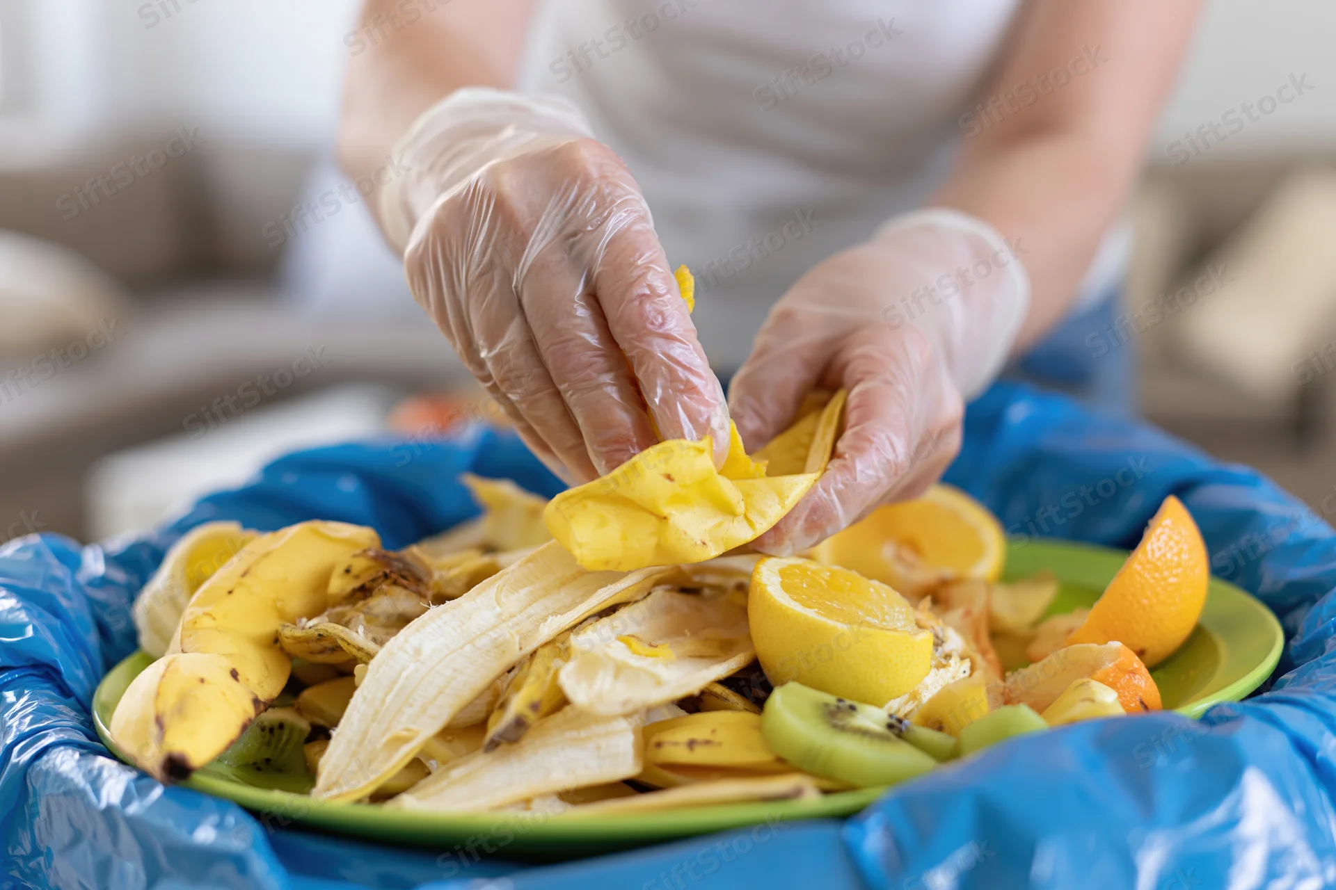Woman in plastic gloves sorting fruit peels into a compost bin