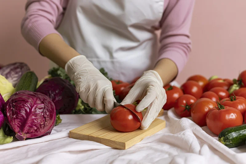 Woman slicing a tomato on a wooden cutting board surrounded by fresh vegetables