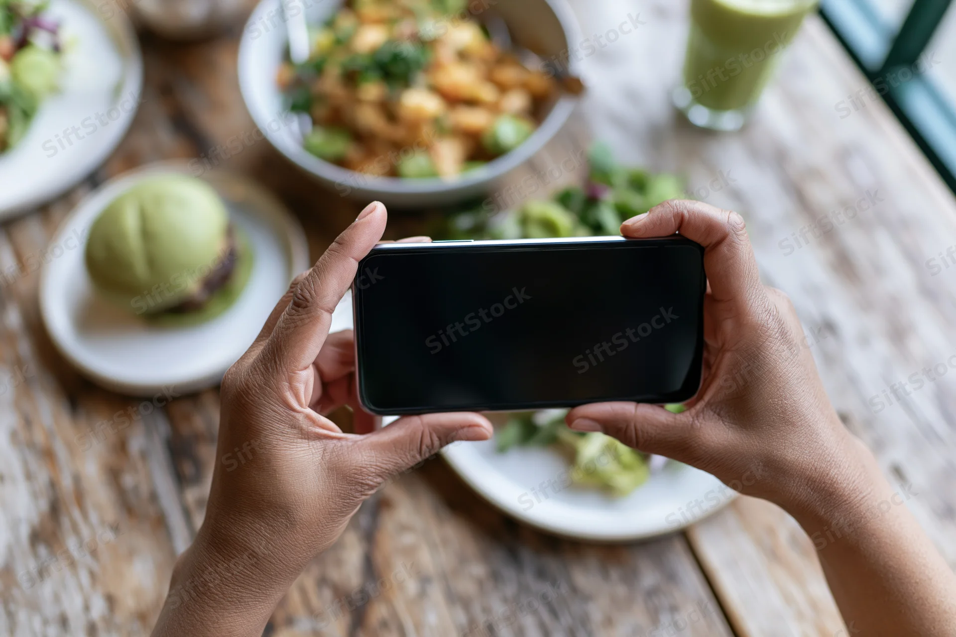 Hands holding smartphone horizontally photographing food on wooden table