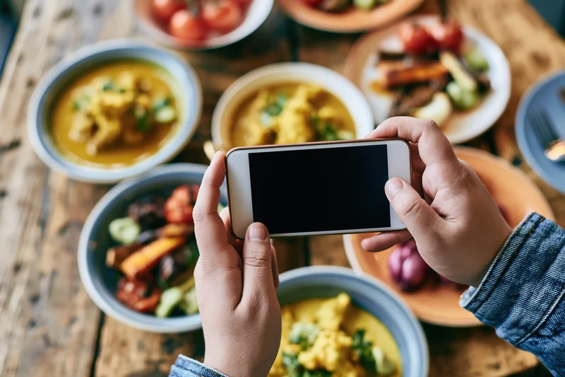 Hands holding smartphone taking photo of food spread on wooden table