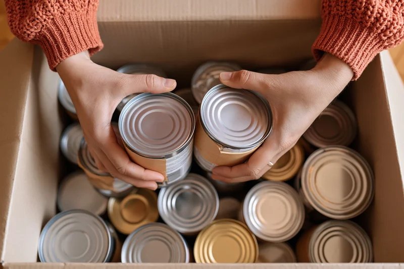 Hands sorting canned food in a cardboard box