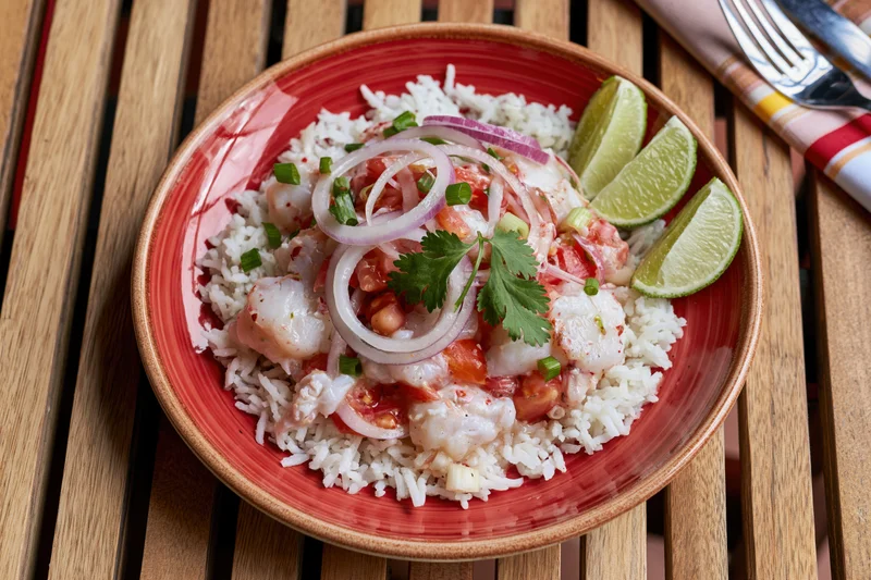 Peruvian ceviche with rice and lime garnish on a red ceramic plate on wooden table