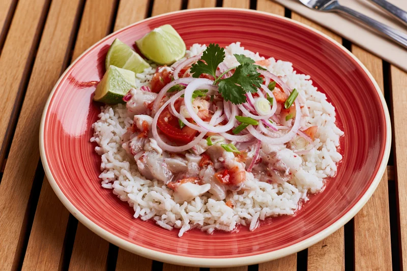Peruvian ceviche with rice and lime garnish on a red ceramic plate on wooden table