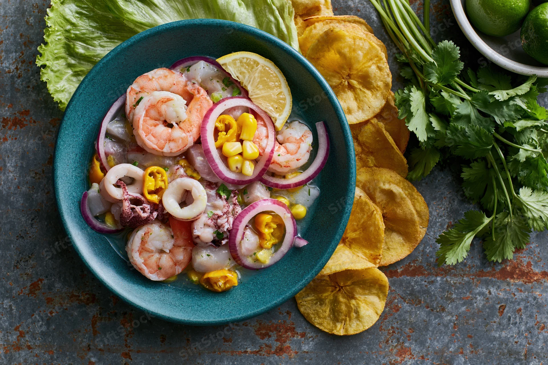 Peruvian seafood ceviche mixto in a teal ceramic bowl with garnishes and chips on a rustic surface