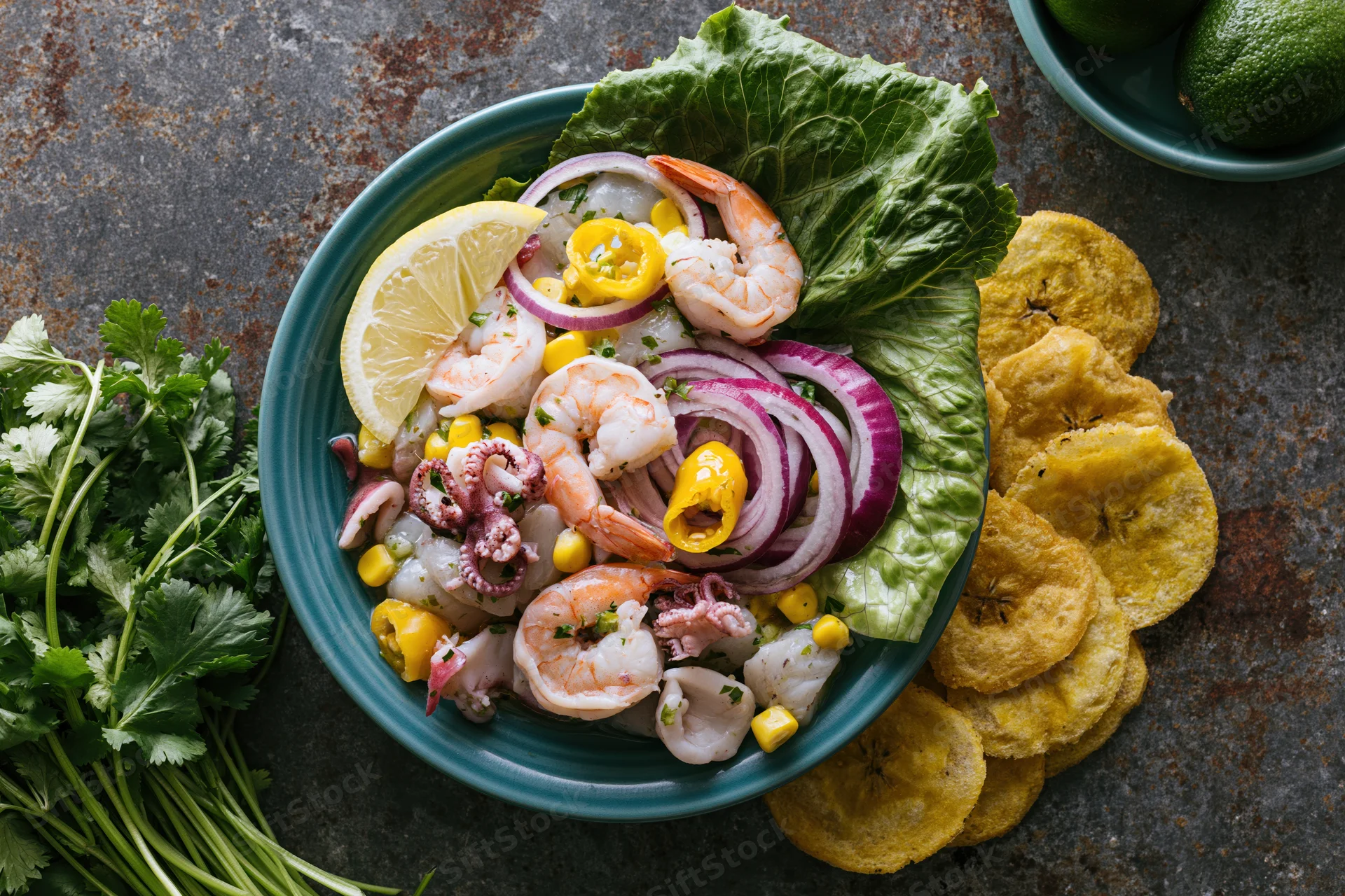 Peruvian seafood ceviche mixto in a teal ceramic bowl with lemon, onion, pepper, lettuce, cilantro, and fried plantain on a dark textured surface