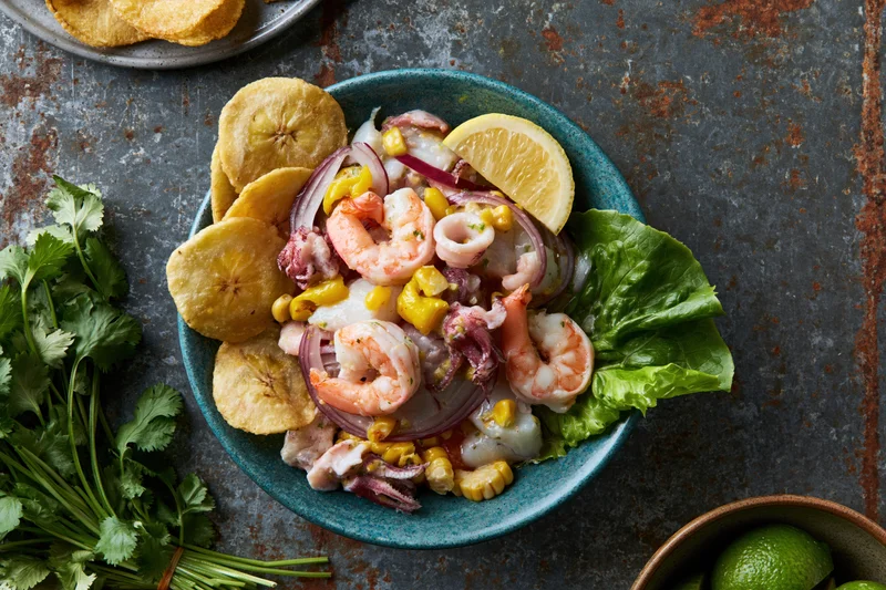 Peruvian seafood ceviche mixto in a teal ceramic bowl with plantain chips and cilantro on a rustic metal table