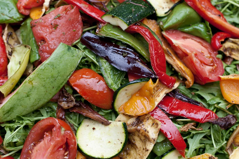 Grilled vegetables and arugula salad with charred peppers and zucchini slices arranged in a pile