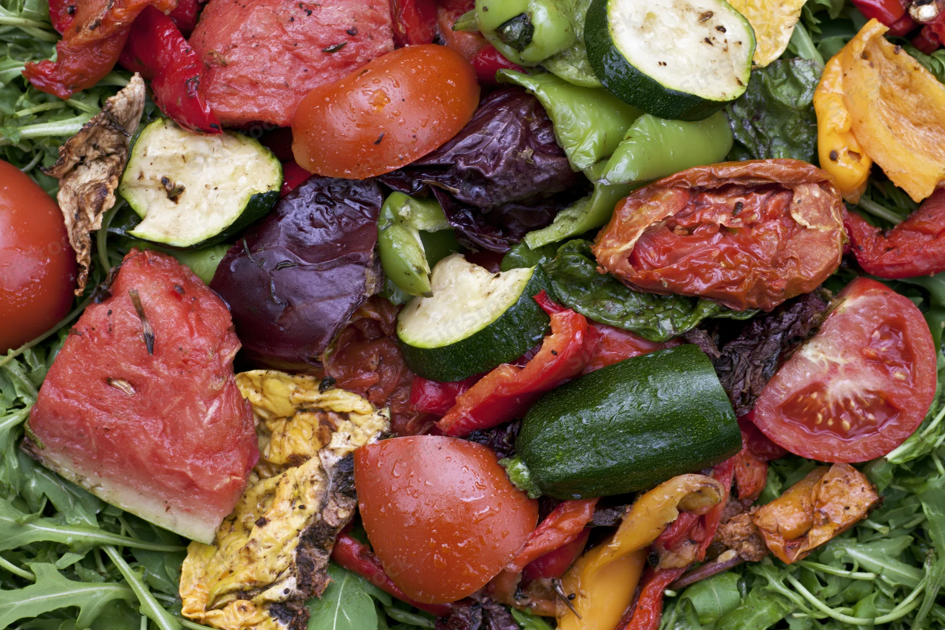 Mixed roasted vegetables and fruit on a bed of arugula, close-up overhead view
