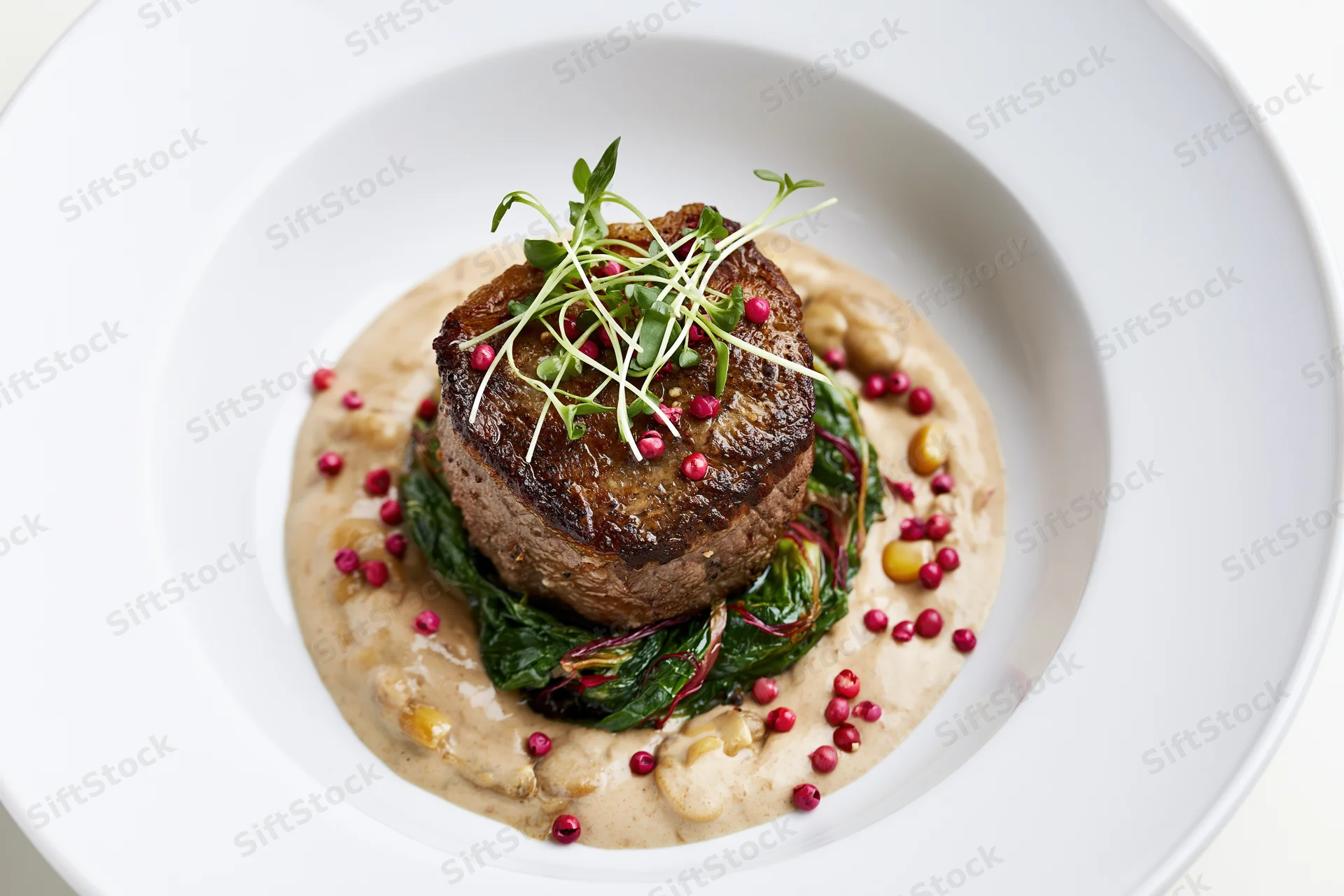Seared beef steak on greens with sauce and garnish in white ceramic bowl