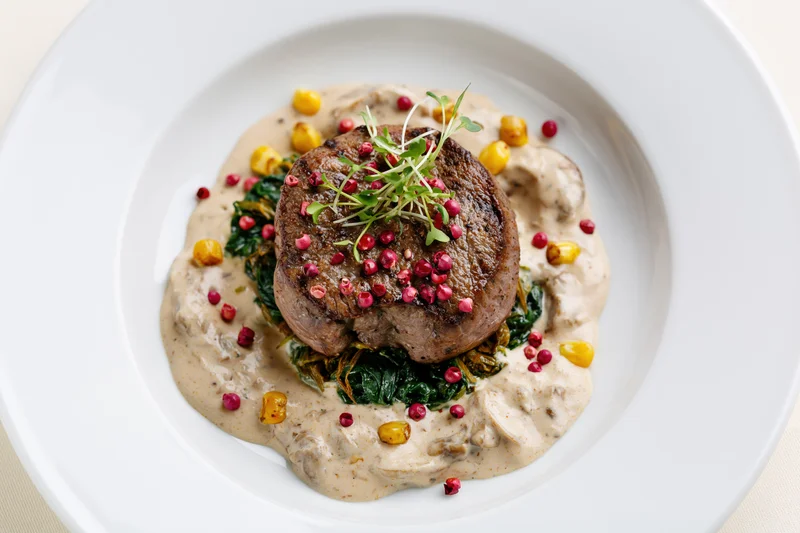 Seared beef steak on cream sauce with spinach and garnish on white plate