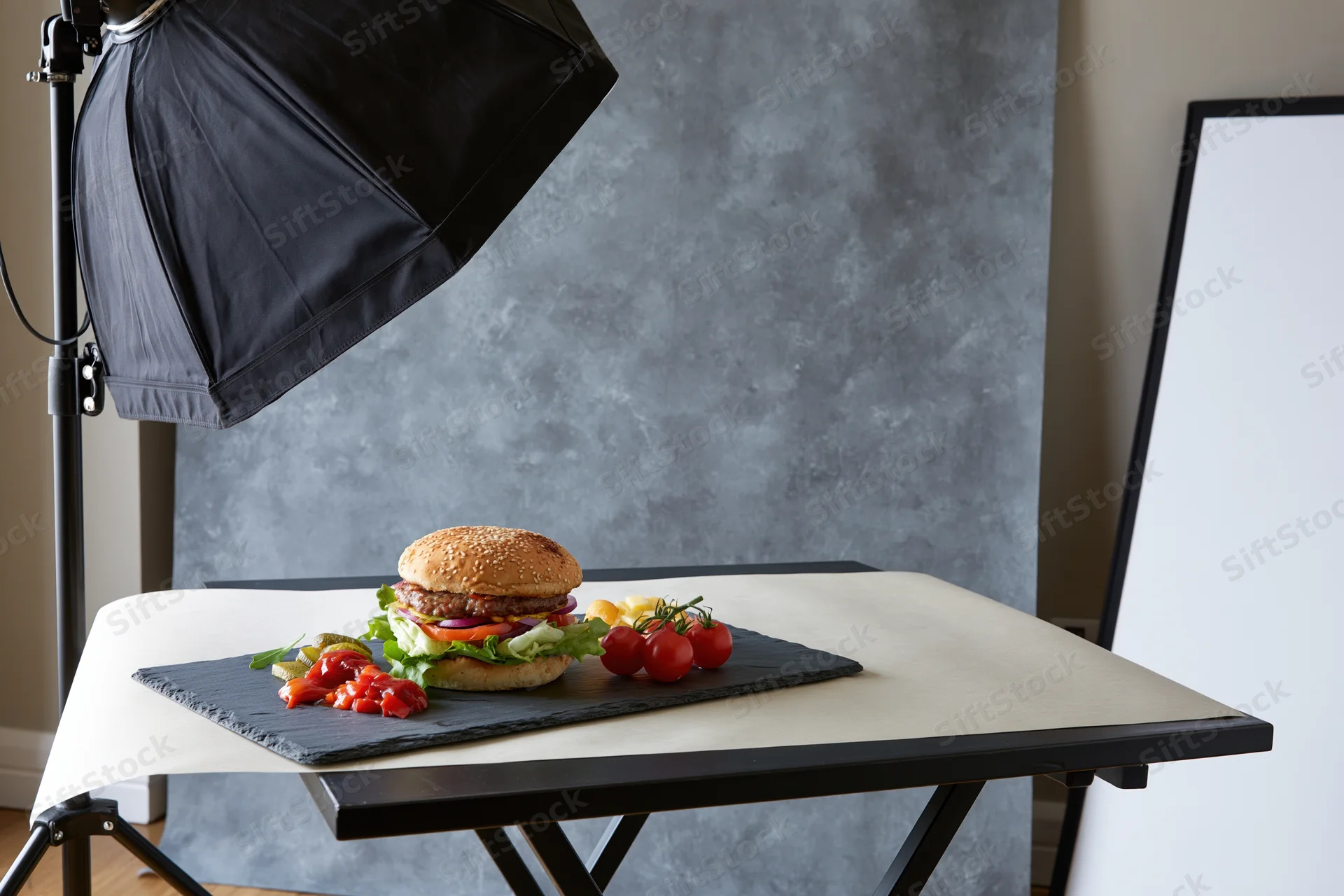 Burger with fries and vegetables arranged on slate board under studio lighting in photography studio
