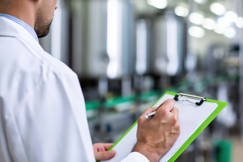 Technician in white lab coat writing on clipboard in industrial facility