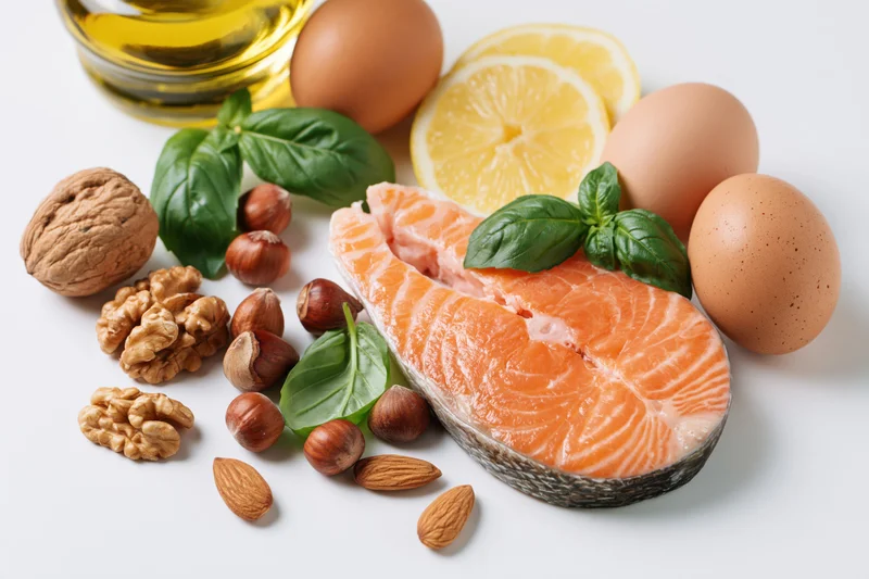 Raw salmon steak with fresh basil, nuts, eggs, lemon and olive oil arranged on white surface
