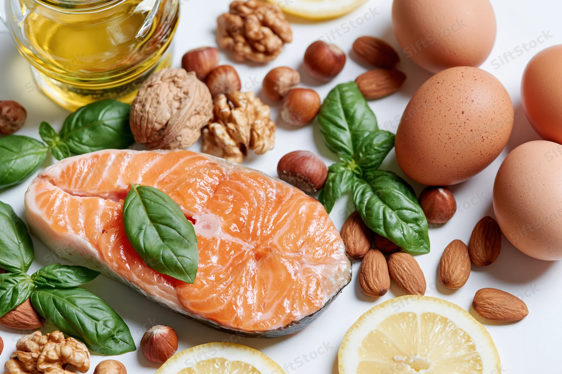 Raw salmon steak with basil, nuts, eggs, lemon, and oil arranged on white surface
