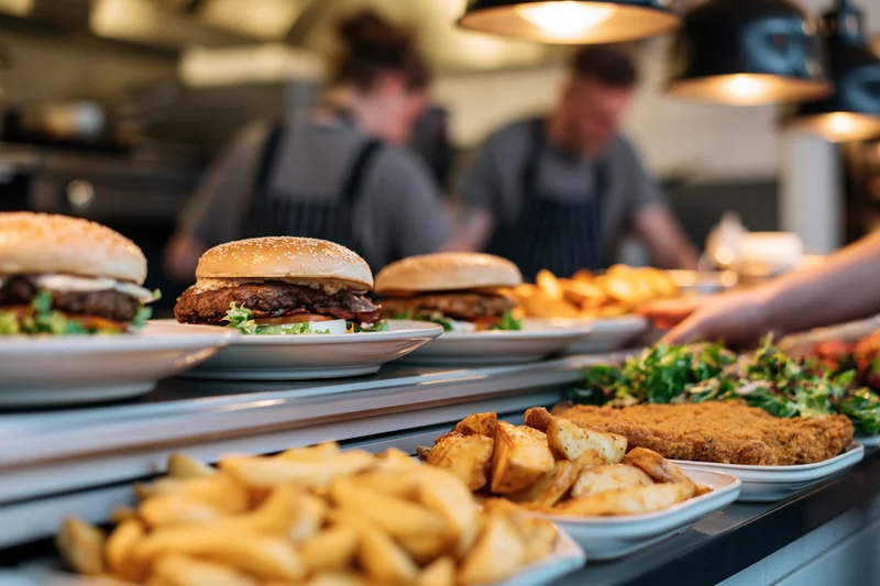 Plated burgers and fries on a restaurant pass counter with chefs in the background