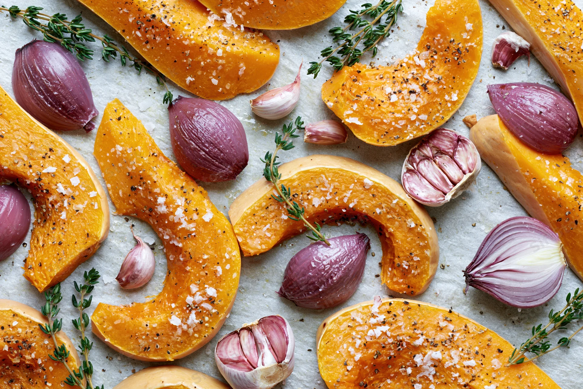 Roasted butternut squash wedges with garlic, shallots and thyme on parchment paper