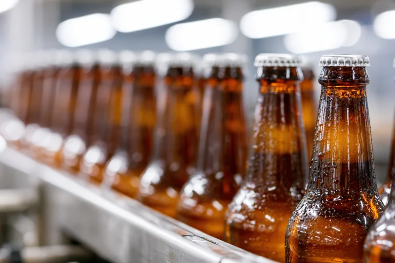 Amber glass beer bottles with silver caps moving along a conveyor in a brewery production line