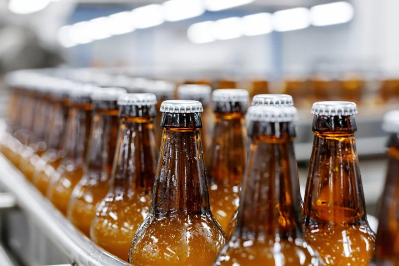 Amber glass beer bottles with silver caps moving along a conveyor in a factory