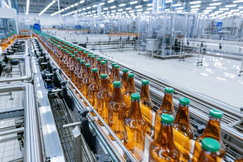 Amber glass bottles with green caps moving along conveyor belt in factory
